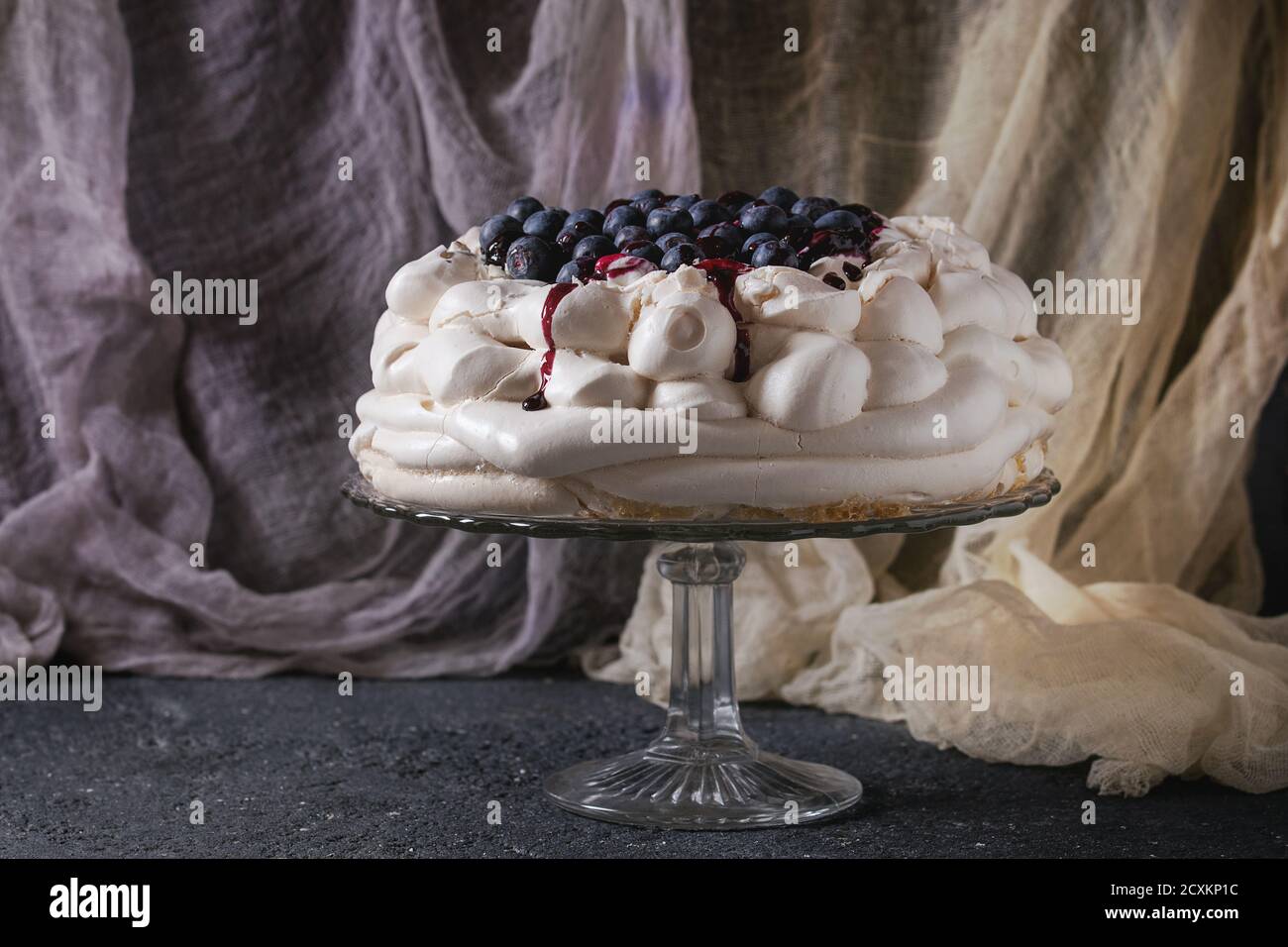 Hausgemachtes Baiser Kuchen Pavlova mit Schlagsahne, frische Heidelbeeren und Blaubeerensauce auf Vintage Etagere auf schwarzen Betontextur Hintergrund, g Stockfoto