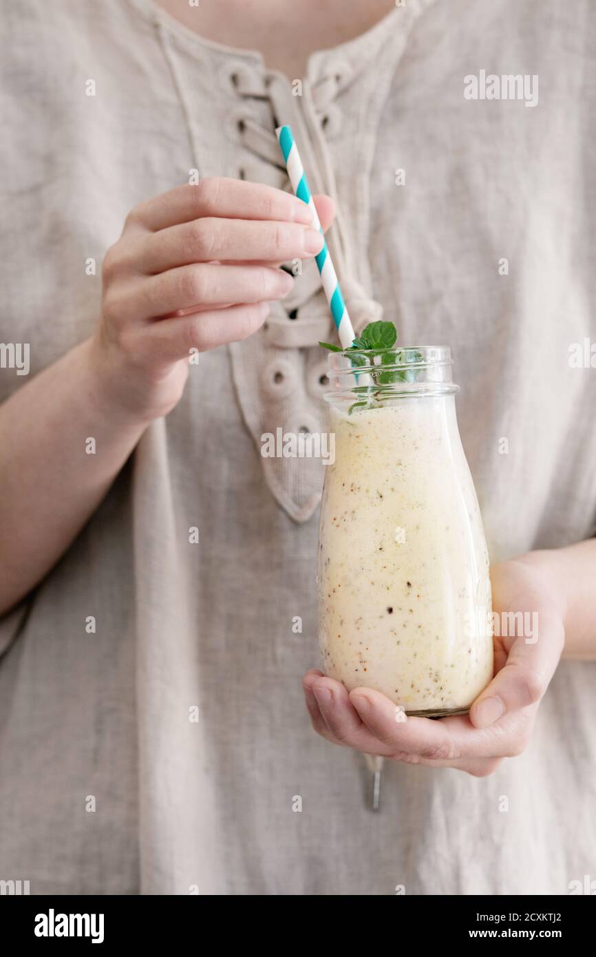 Eine Flasche Smoothie mit Chia-Samen, Heidelbeeren, Minze und retro gestreiftes cocktail Rohr in weiblichen Händen. Frau in weißem Leinen Kleid. Gesunde eati Stockfoto