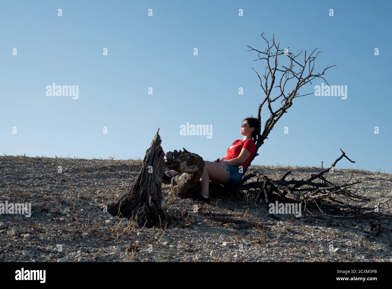 Junge Frau, die auf einem trockenen Baumstamm auf dem Wüstenhügel sitzt. Trockenes Land kein Wasser. Nikosia Zypern Stockfoto