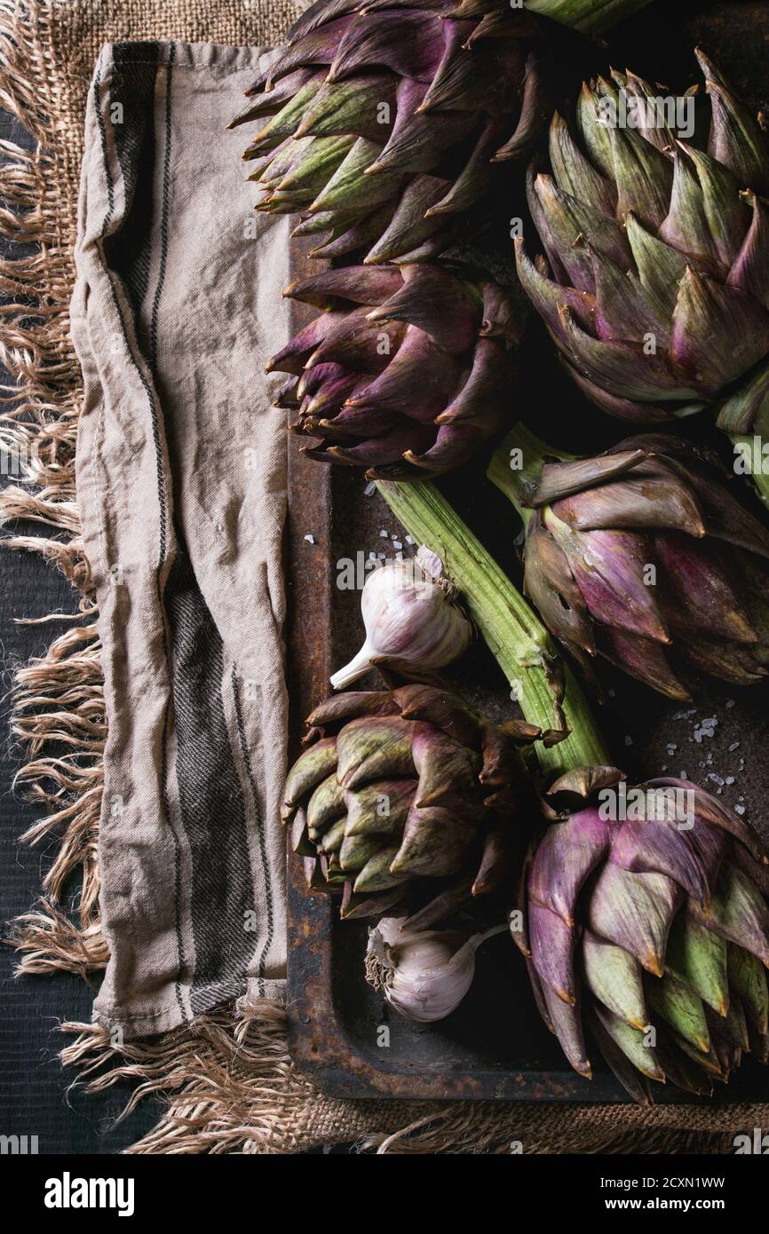 Rohem ganz Bio nass lila Artischocken mit Knoblauch in alten rostigen Backblech auf Textile Sackleinen in dunklem Holz. Rustikalen Stil. Top vi Stockfoto