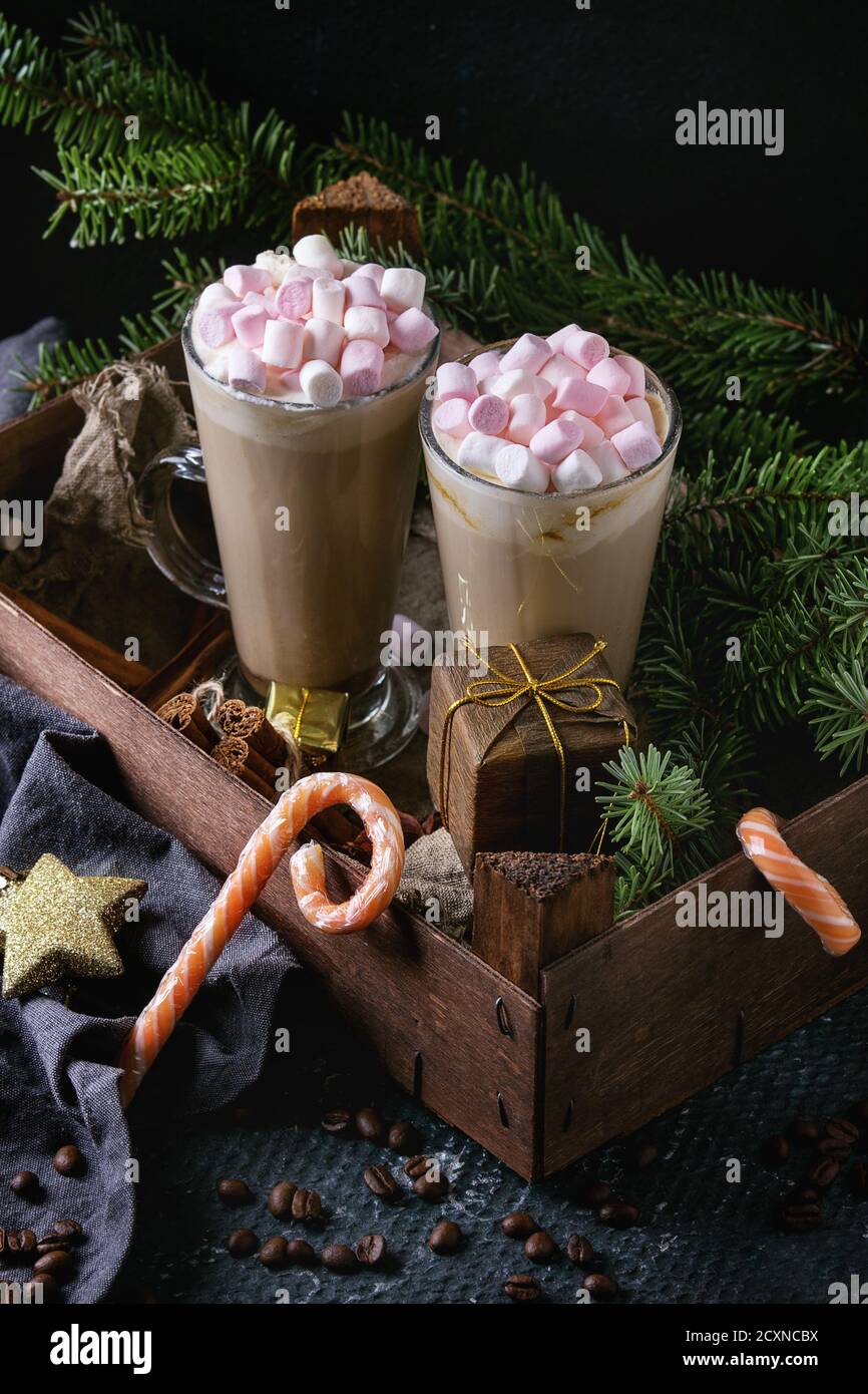 Zwei Gläser Café Latte mit rosa Marshmallow stehen in Holzkiste mit Weihnachtsdekor, Süßigkeiten, Gewürzen, Kaffeebohnen und Tannenbaum über dunklem Text Stockfoto