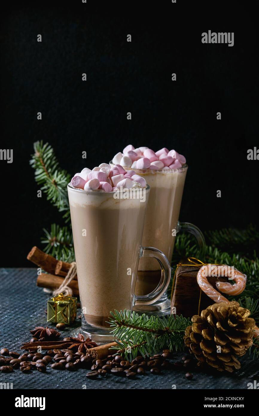 Zwei Gläser Café Latte mit rosa Marshmallow mit Weihnachten Dekor, Bonbons, Gewürze, Kaffee-Bohnen und Tanne über dunkle Textur Hintergrund. Top vie Stockfoto