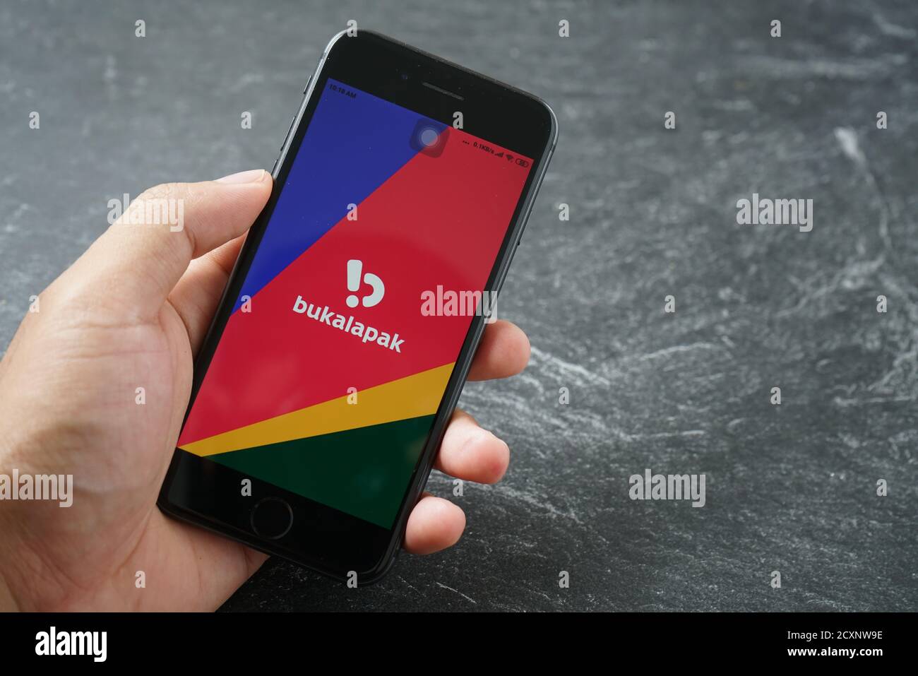 Mataram, Indonesien - 1. Oktober 2020: Hand hält Apple iPhone 8 mit bukalapak Marktplatz Online-Shop auf dem Bildschirm auf Stein Pad, Draufsicht. Stockfoto