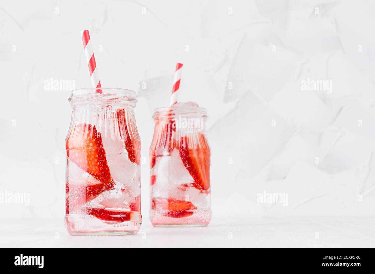 Kaltes frisches Fruchtgetränk von reifen Erdbeeren mit Eis, Sodawasser, Blasen, lustig gestreiftem Stroh auf einfachem weichen hellen weißen Hintergrund, Kopierraum. Stockfoto