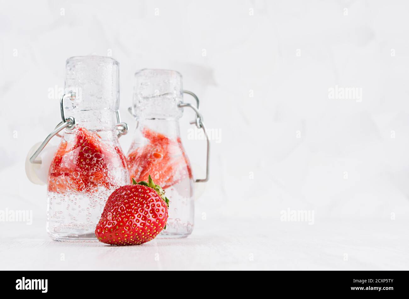 Frische Sommercocktails mit reifen Erdbeeren, Soda, hellen Blasen in zwei Joch-Flaschen auf elegantem, hellweißem Holzbrett und Gipswand. Stockfoto