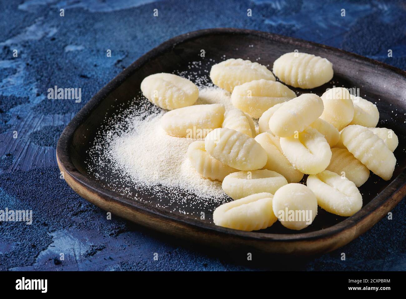 Rohe Kartoffelgnocchi in schwarzen Holzteller mit Mehl auf dunkelblauem Betongrund. Nahaufnahme mit Raum. Hausmannskost. Stockfoto