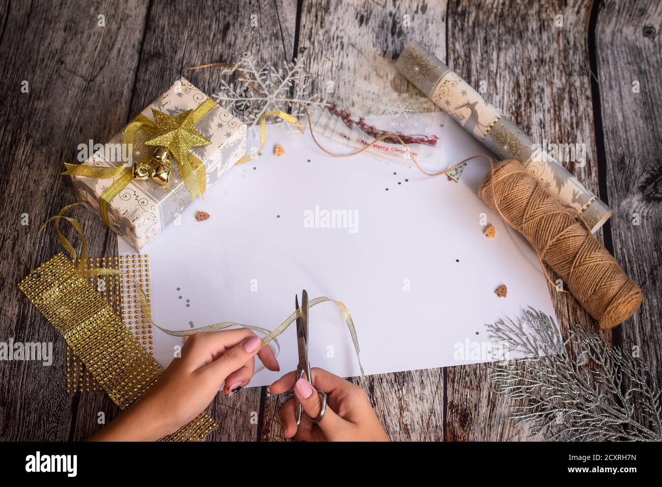 Vorbereitung auf Weihnachten. Die Hände des Mädchens schneiden das Band für Flat Lay mit einer Schere. Weißes leeres Blatt in der Mitte für die Inschrift. Stockfoto