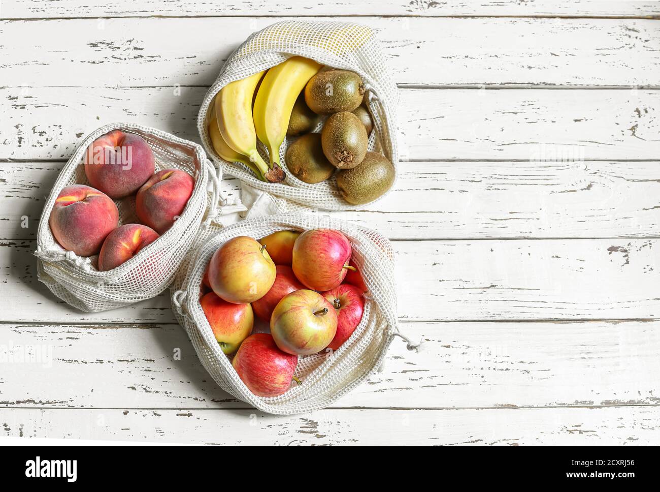 Äpfel, Pfirsich, Kiwi, Bananen in wiederverwendbaren, umweltfreundlichen Netztüten auf weißem Holzhintergrund. Zero Waste Konzept und Kunststoff frei Lebensstil. Stockfoto