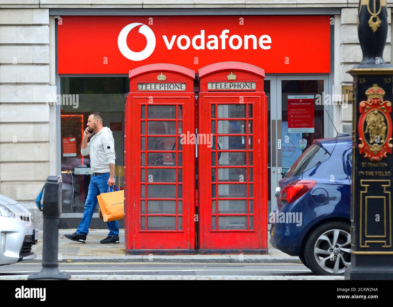London, England, Großbritannien. Traditionelle rote Telefonzellen vor einem Vodafone-Shop, The Strand. Stockfoto