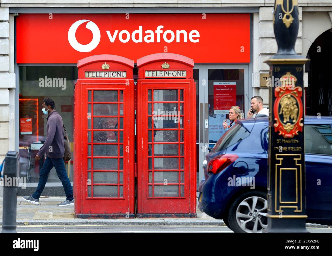 London, England, Großbritannien. Traditionelle rote Telefonzellen vor einem Vodafone-Shop, The Strand. Stockfoto