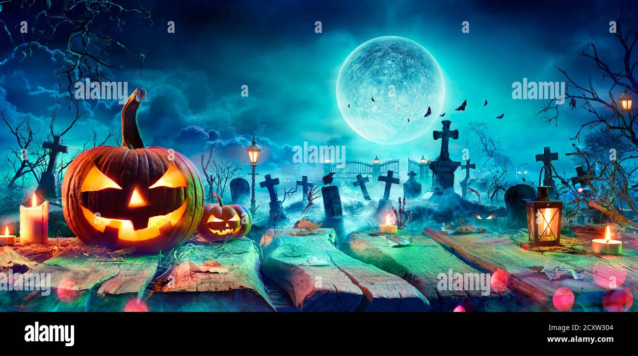 Jack O’ Laterne auf dem Tisch in gruseligen Friedhof in der Nacht - Halloween Mit Vollmond Stockfoto