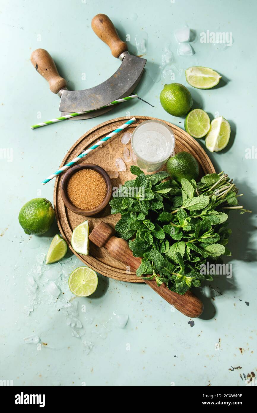 Zutaten für die Herstellung von mojito Cocktail. Frische Minze, Limette, brauner Zucker, crashed ice cubes, Glas Sodawasser, cocktail Rohre auf Holzbrett über gr Stockfoto