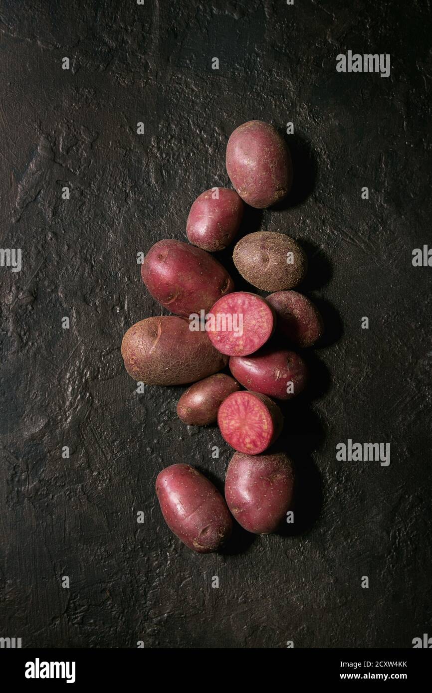 Roh ungekocht Biokartoffeln namens lilu Rose, ganze und Schicht über dunkle Textur Hintergrund. Ansicht von oben, kopieren Raum Stockfoto