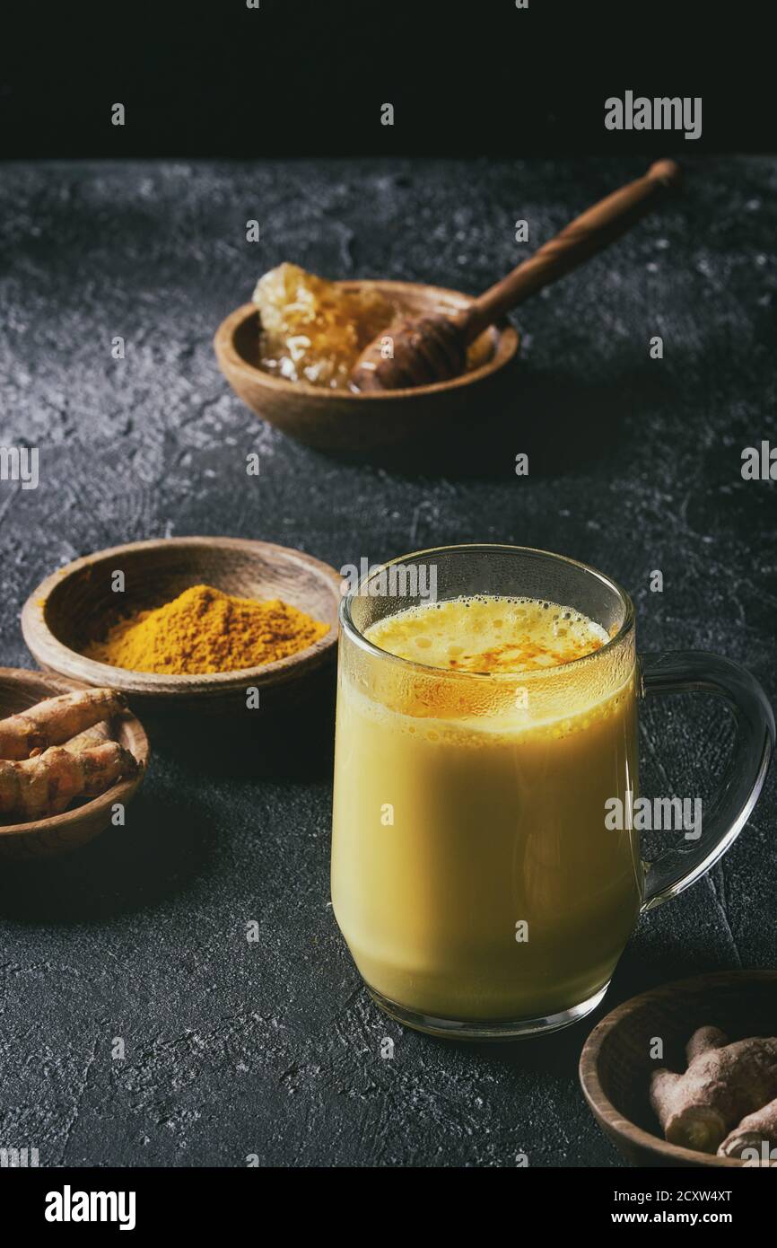 Tasse ayurvedischen Getränk golden Milch Latte mit Gelbwurz Kurkuma Pulver und Zutaten oben über schwarze Textur Hintergrund. Getonten Bild Stockfoto