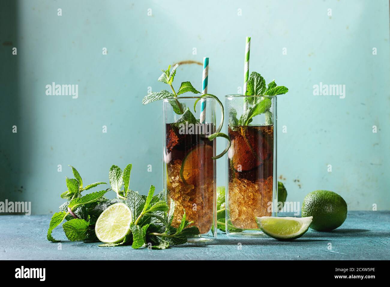 Zwei Gläser classic Cuba Libre Cocktail mit Limetten, Minze, crushed Eis und Cola, serviert mit Zutaten oben und retro cocktail Rohre über Türkis Stockfoto