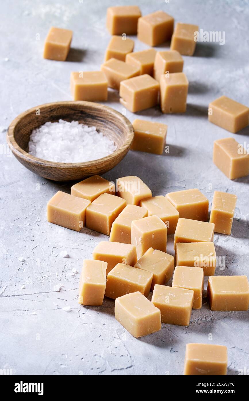 Gesalzene caramel fudge Candy auf Holzbrett mit Fleur de Sel in Houten über grau Textur Hintergrund serviert. Nahaufnahme Stockfoto