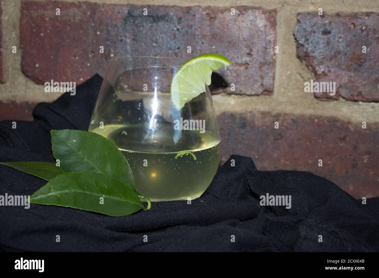 Gin und Tonic auf einem schwarzen Material gegen eine rustikale Ziegelwand, mit garniert mit einem Stück Limette Stockfoto