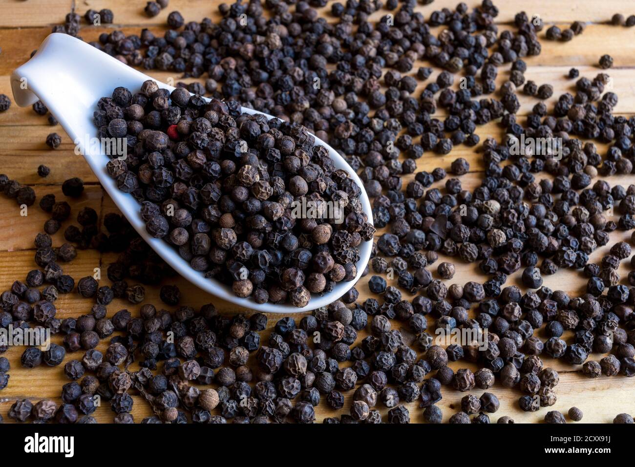 Trockene schwarze Pfefferkörner im Gewichtlöffel Stockfoto