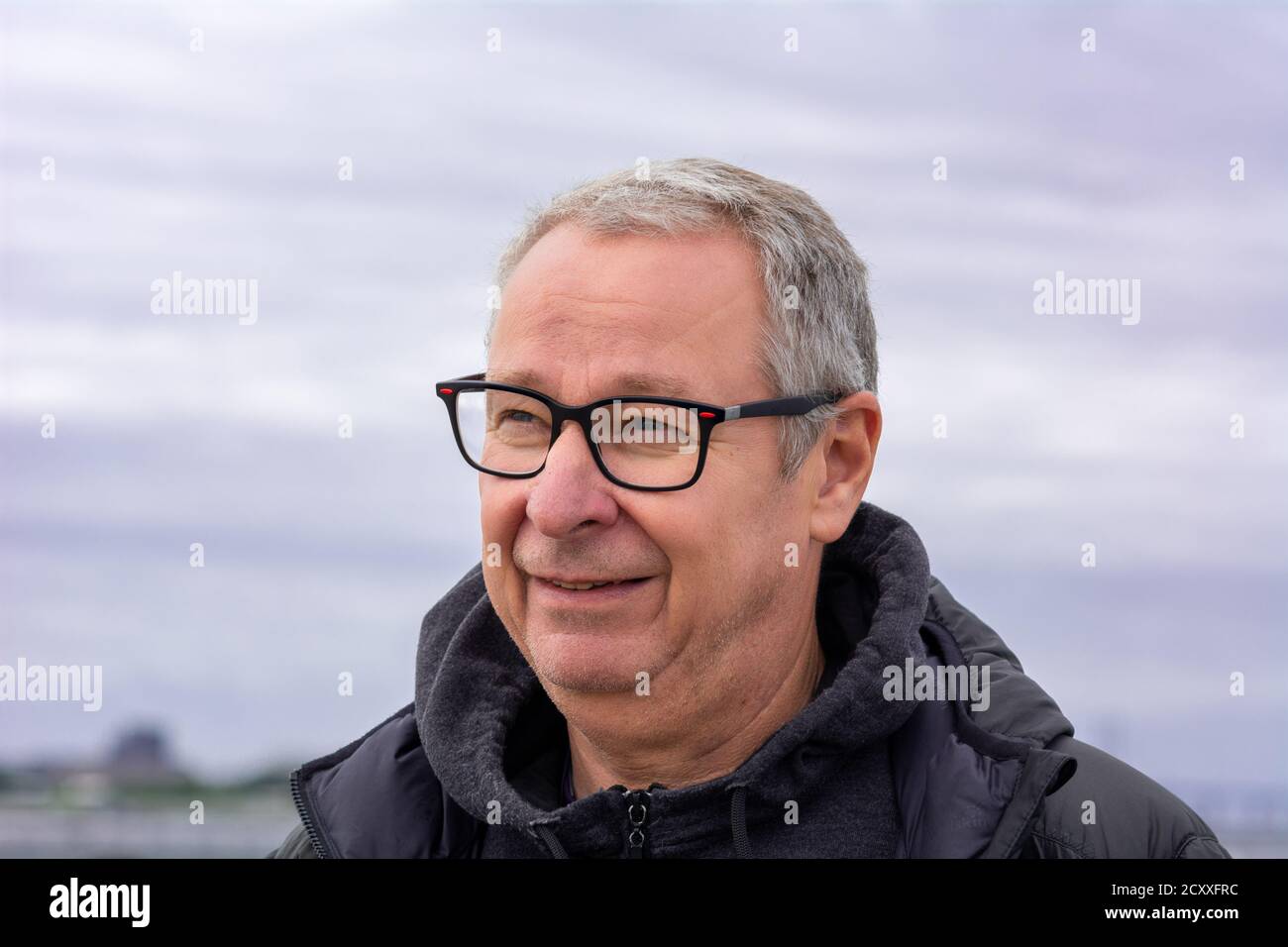 Nahaufnahme eines Mannes mittleren Alters, um die 50, mit grauen Haaren und Brille. Blauer Dunsthimmel im Hintergrund Stockfoto