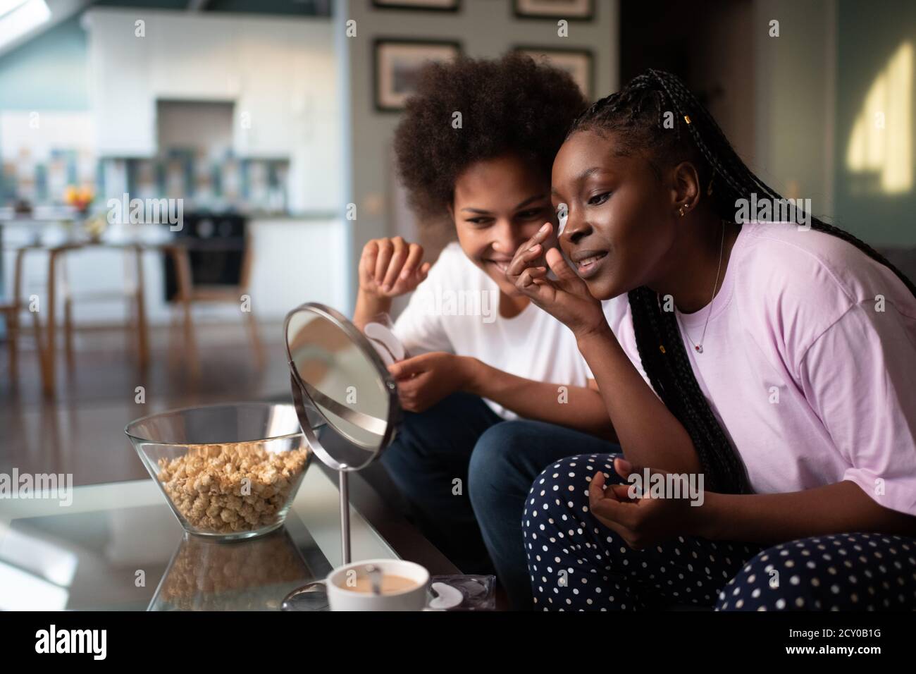 Multiethnische Freundinnen mit unter den Augenpolstern lächelnd und anblickend Spiegel zu Hause Stockfoto