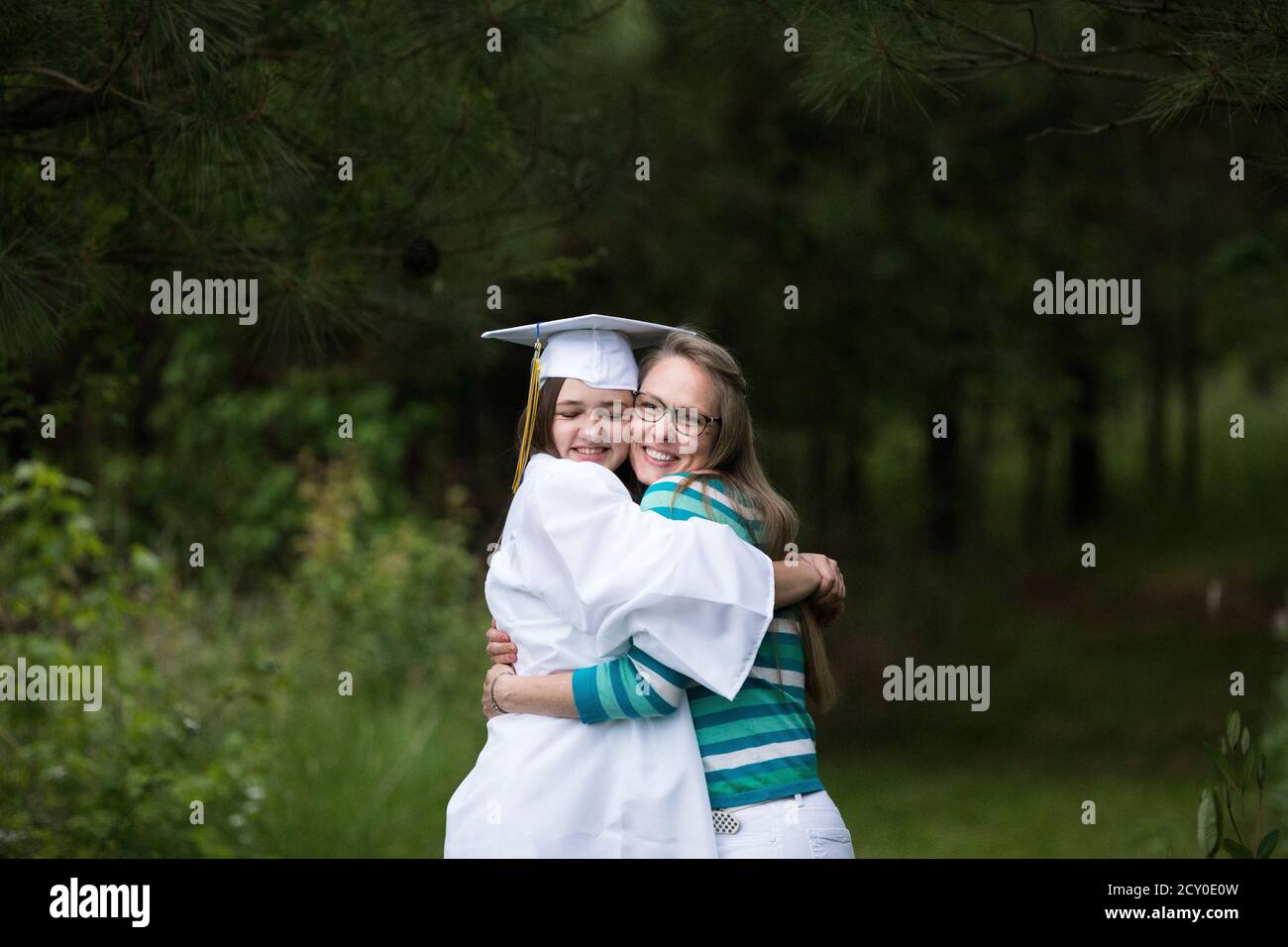 Glücklich weibliche Graduate trägt weiße Kappe und Gown eng Hugs Ihre Mutter Stockfoto