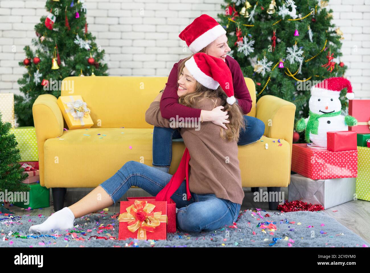 Hugs Freunde Mädchen Freundinnen geben Neujahr Geschenk in Box, lächeln und lachen, im Hintergrund ist Weihnachtsbaum. Konzept-Sisterhaube. Stockfoto