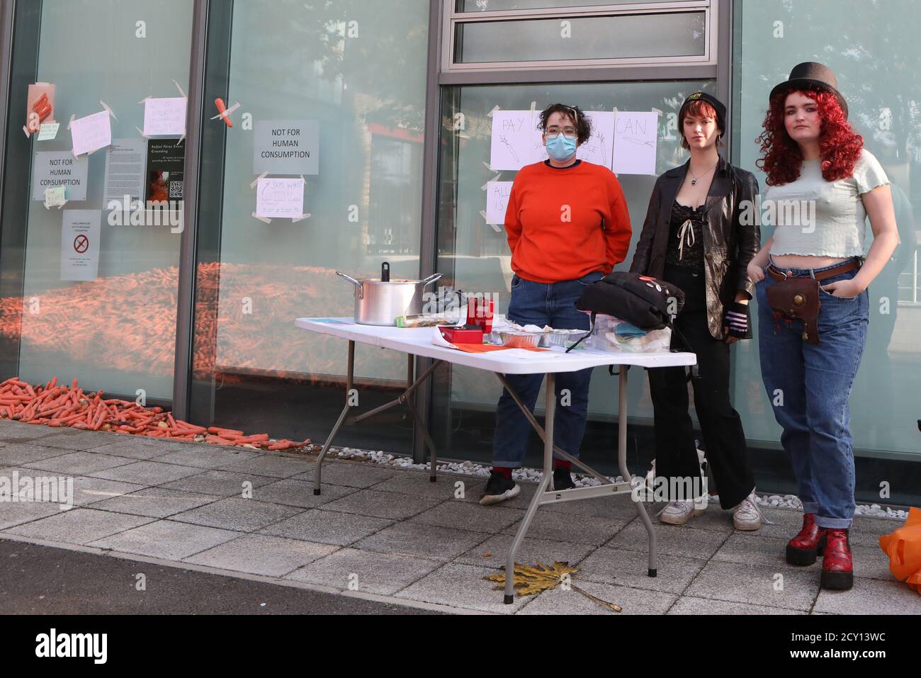 (Von links nach rechts) Yasmine Metcalfe, Rebecca Fall und Nancy Violet O'Brien protestieren gegen die 29 Tonnen Karotten, die vor dem Goldsmiths College in London - für eine Kunstinstallation mit dem Titel "Grounding" von Rafael Perez Evans - übrig geblieben sind, indem sie aus den Karotten Lebensmittel machen und den Erlös an Wohltätigkeitsorganisationen spenden. Stockfoto
