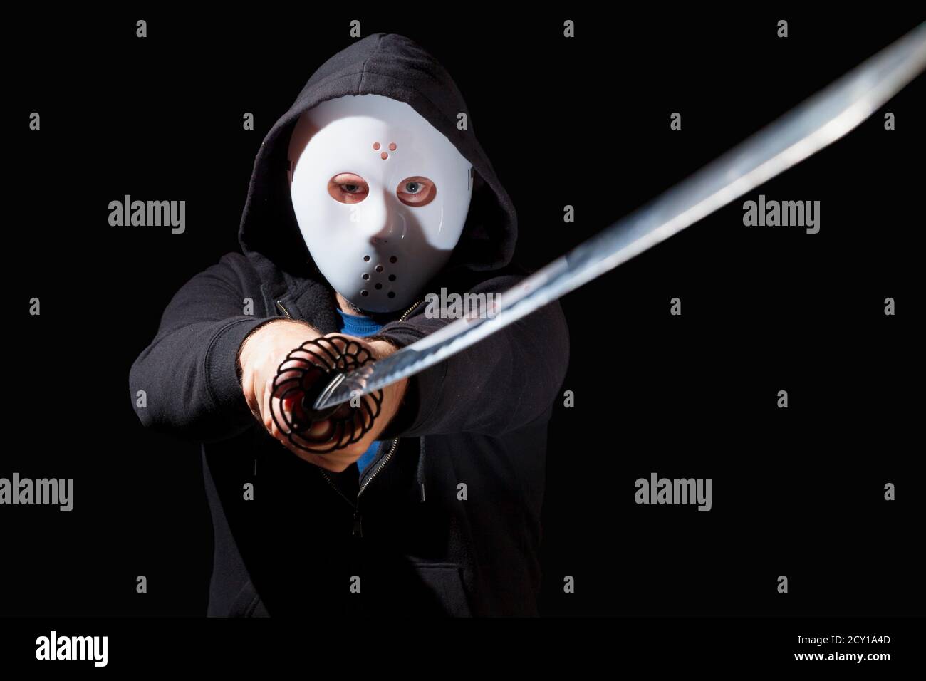 Mann bewaffnet mit einem Katana und trägt eine Hockey-Maske und ein Hoodie auf schwarzem Hintergrund. Stockfoto