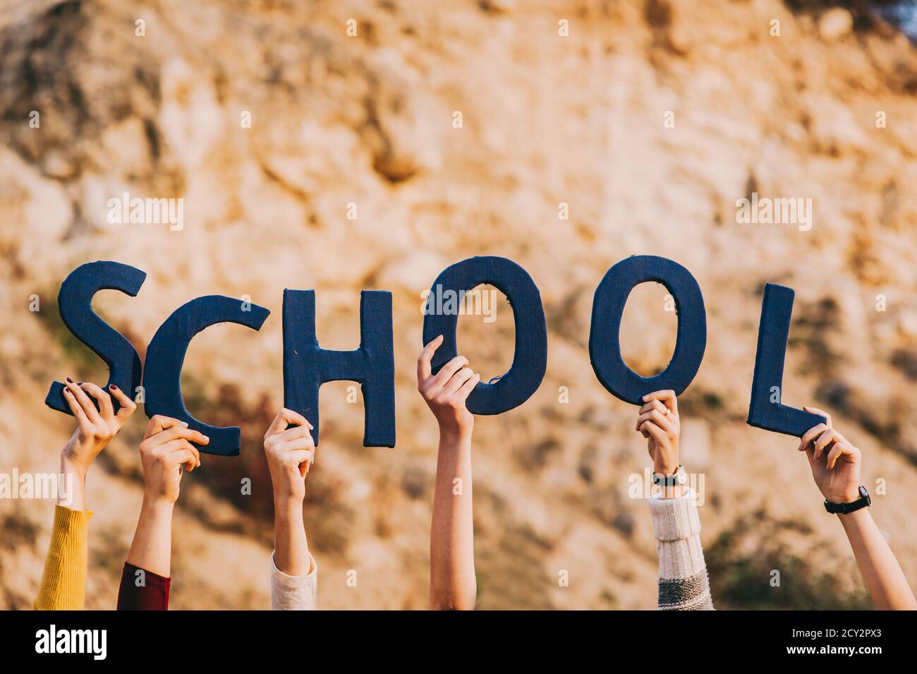 Erhobene Hände von gesichtslosen Jungen und Mädchen halten blaue Buchstaben, wie sie die Inschrift Schule bilden. Stockfoto