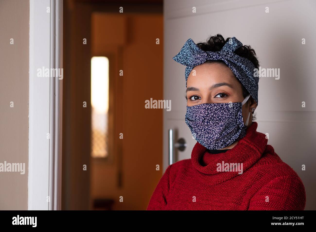 Portrait vonseriousafrikanisch-amerikanischer Frauenmit passendem Stirnband und Gesichtsmaskenbetrachend der Kamera. Am Hauseingang. Mode, Individualität, Trend, Ident Stockfoto