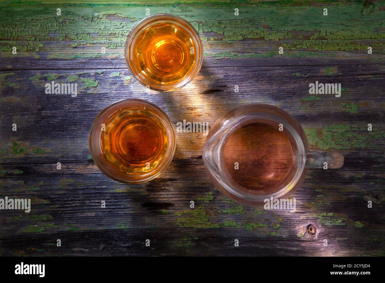 Foto von Glas und zwei Gläsern Getränk auf verfallenen Holztisch Stockfoto