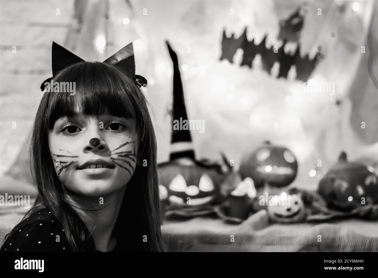 Begeistert von Halloween. Schwarz-Weiß-Foto von niedlichen Teenager-Mädchen in schwarz Katze Kostüm und geschnitzten Kürbis auf dem Hintergrund Stockfoto
