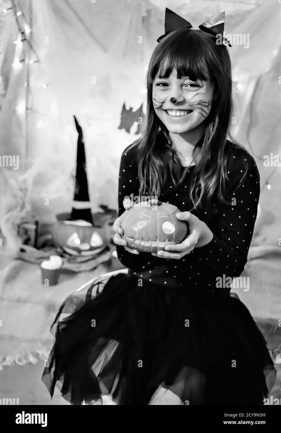 Halloween-Heimparty. Schwarz-Weiß-Porträt von niedlichen lächelnden Mädchen in schwarz Katze Kostüm und geschnitzten Kürbis in den Händen Stockfoto
