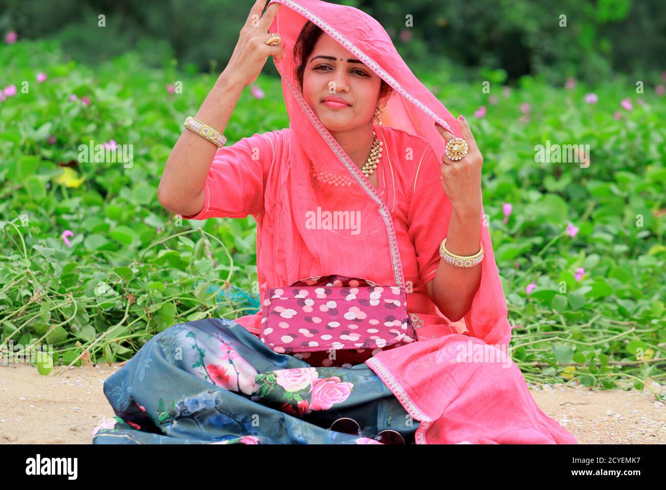 Eine indische Erwachsene Modekünstlerin Frau sitzt im Garten, heben den Schleier mit ihrer Hand und schaut weg mit einem lächelnden Gesicht Stockfoto