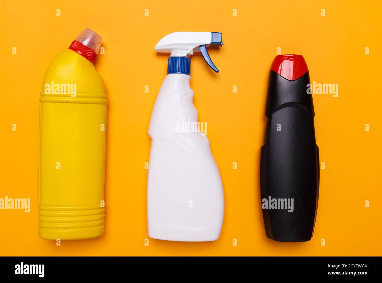 Eine gelbe Flasche mit einem Toilettenreiniger sowie eine weiße Flasche zum Reinigen von Glas und eine schwarze Flasche zum Entfernen von Rost auf gelbem Hintergrund. Stockfoto