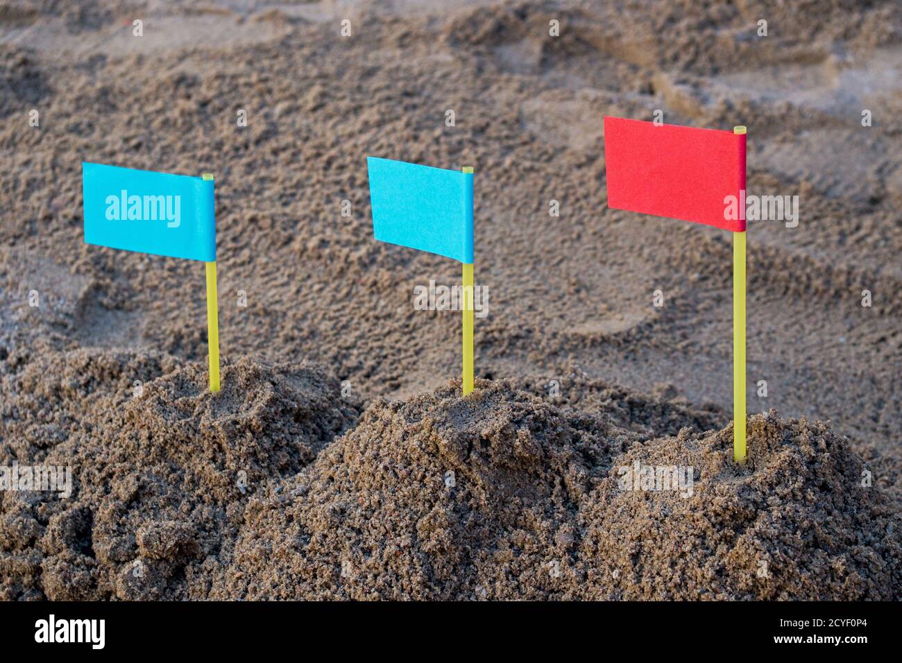 Im Sandkasten drei Sandhügel von links nach rechts mit zwei blauen Fahnen auf der linken und roten Flagge auf der rechten Seite. Konzept: Führung in der Geschäftsstrategie Stockfoto