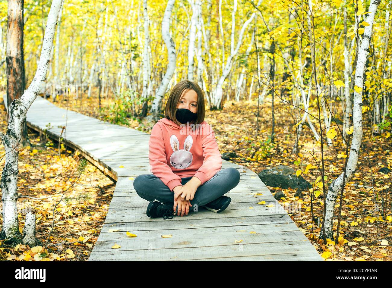 Ein niedliches 7-8 Jahre altes Mädchen in schwarzer Maske im Herbstwald. Outdoor Lifestyle, Aufenthalt, Quarantänezeit. Herbst Stockfoto