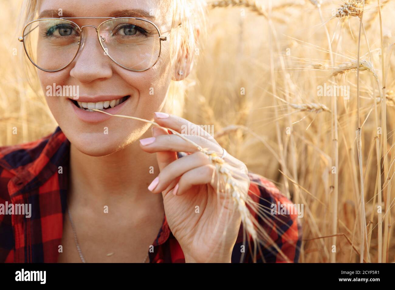 Eine Frau mit grauen Augen, die eine Brille und eine rote trägt shirt sitzt auf einem Feld Stockfoto