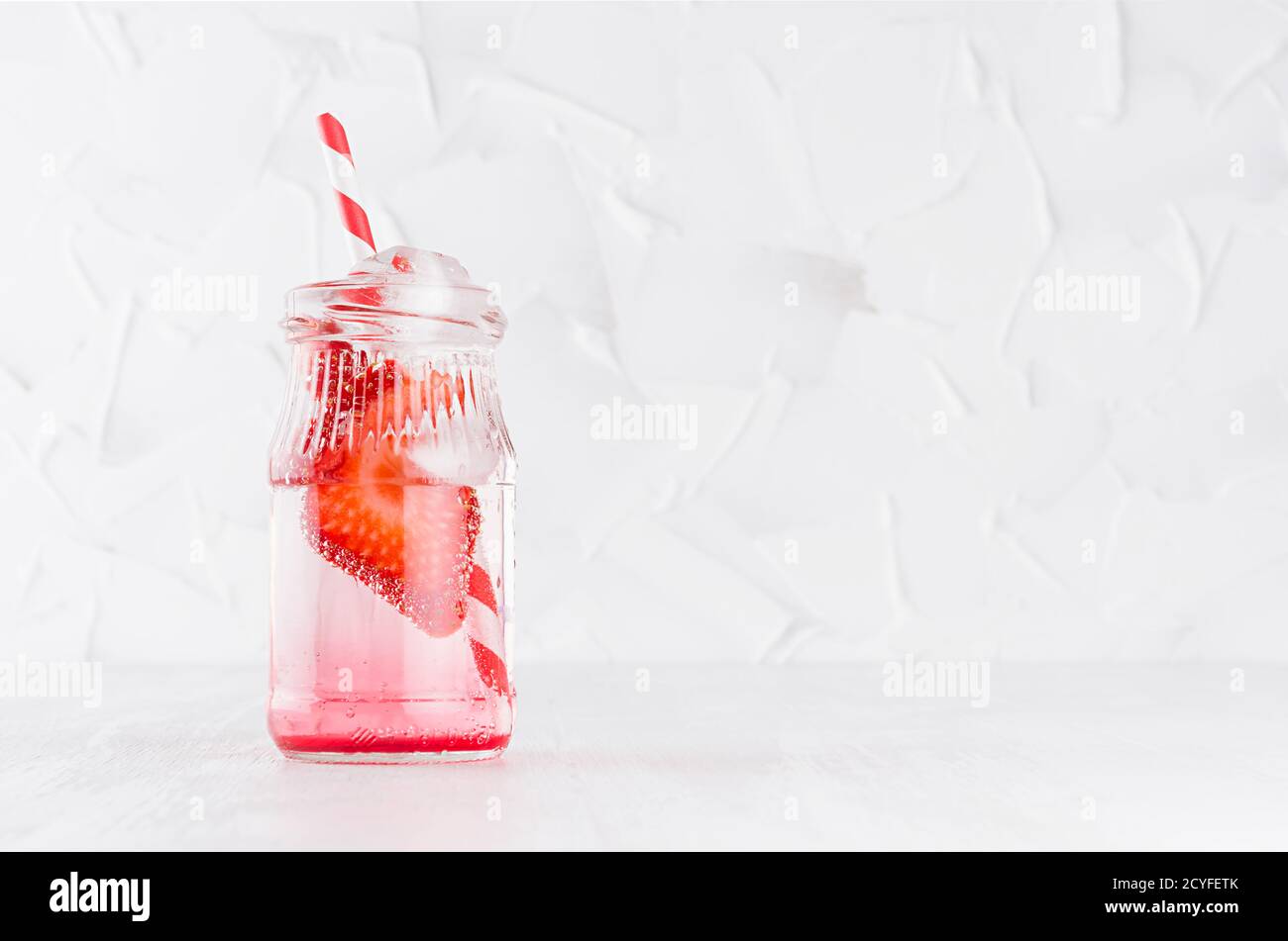 Frischer Sommercocktail mit reifen Erdbeeren, Soda mit Stroh, Eiswürfeln auf eleganter, hellweißer Holzplatte und Gipswand. Stockfoto