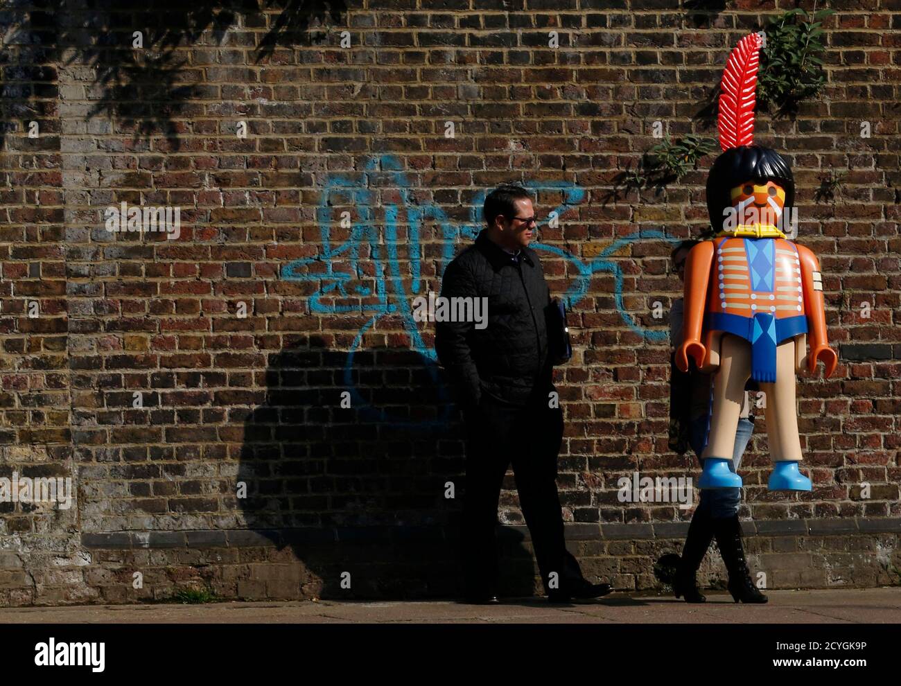 Ein Wachmann schaut zu, wie eine riesige Playmobil-Figur während des Starts  eines Ereignisses zu Playmobil 40. Jubiläum in Camden in London 30. April  2014 durchgeführt wird. 40 lebensgroßen Playmobil-Figuren aus den letzten