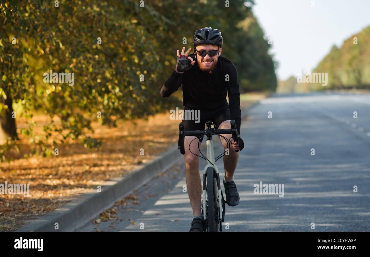 Lächelnder Mann auf einem Rennrad auf der Straße. Radfahren, Training, sich bei körperlicher Aktivität auf einem Schotterfahrrad wohlfühlen Stockfoto