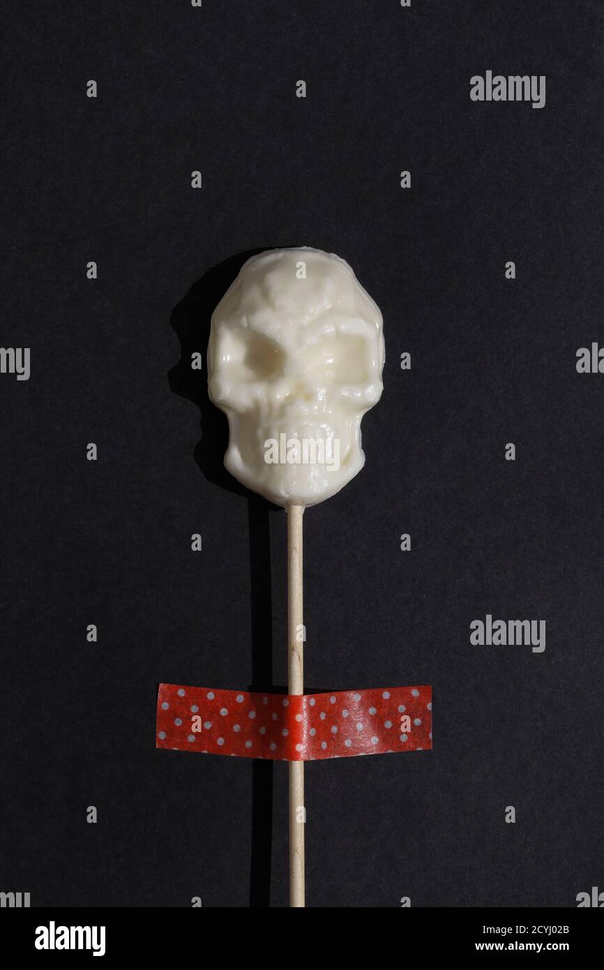 Weißer Lollipop in Form von Schädel auf schwarzem Hintergrund. Kreative Halloween Minimal Konzept. Flach Lay Draufsicht Stockfoto