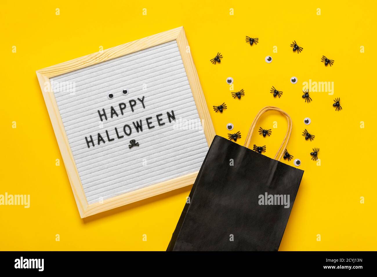 Filzbrett mit Text und schwarzem Paket, krabbelnde Spinnen auf gelbem Hintergrund Draufsicht Flat Lay Happy Halloween Kreativkonzept Weihnachtskarte Stockfoto