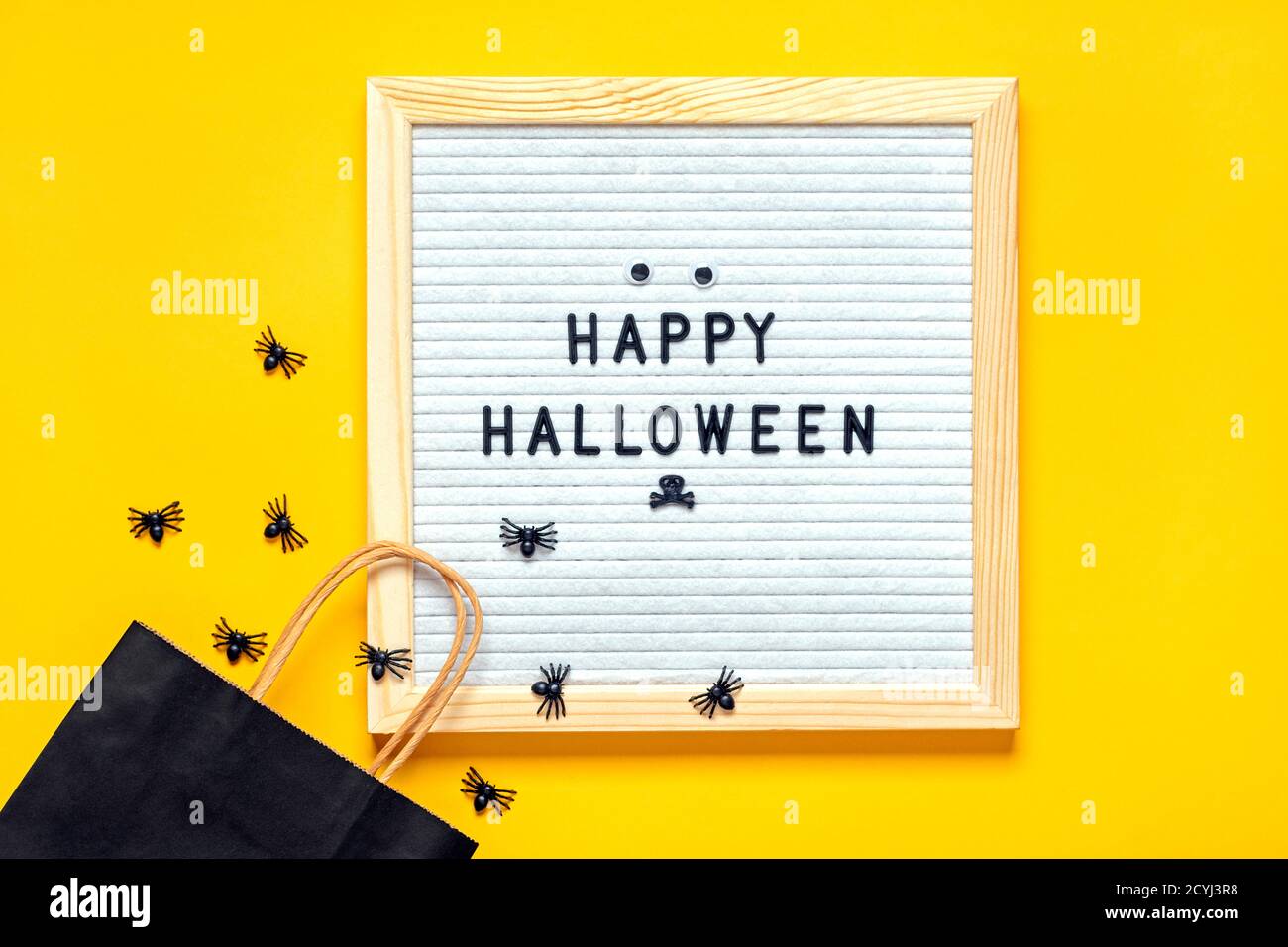 Filzbrett mit Text und schwarzem Paket, krabbelnde Spinnen auf gelbem Hintergrund Draufsicht Flat Lay Happy Halloween Kreativkonzept Weihnachtskarte Stockfoto