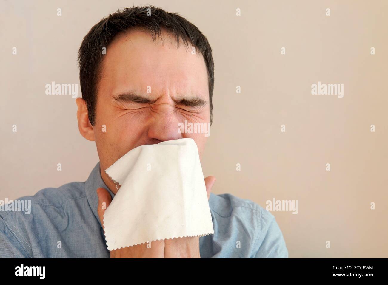 Der Kerl niest in ein Taschentuch Nahaufnahme. Die Ausbreitung von Mikroben und Bakterien. Junger Mann, der seine Nase bläst Stockfoto