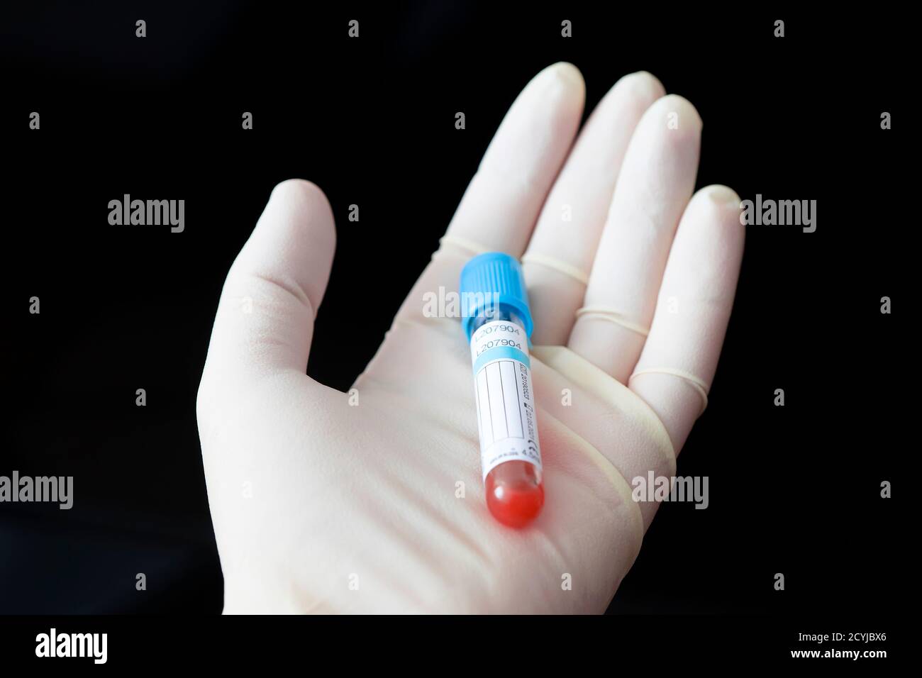 Wissenschaftler hält das Reagenzglas der Blutprobe auf schwarzem Hintergrund, Nahaufnahme mit Platz für Text. Leeres weißes Etikett für den Namen des Patienten oder Bluttest Stockfoto