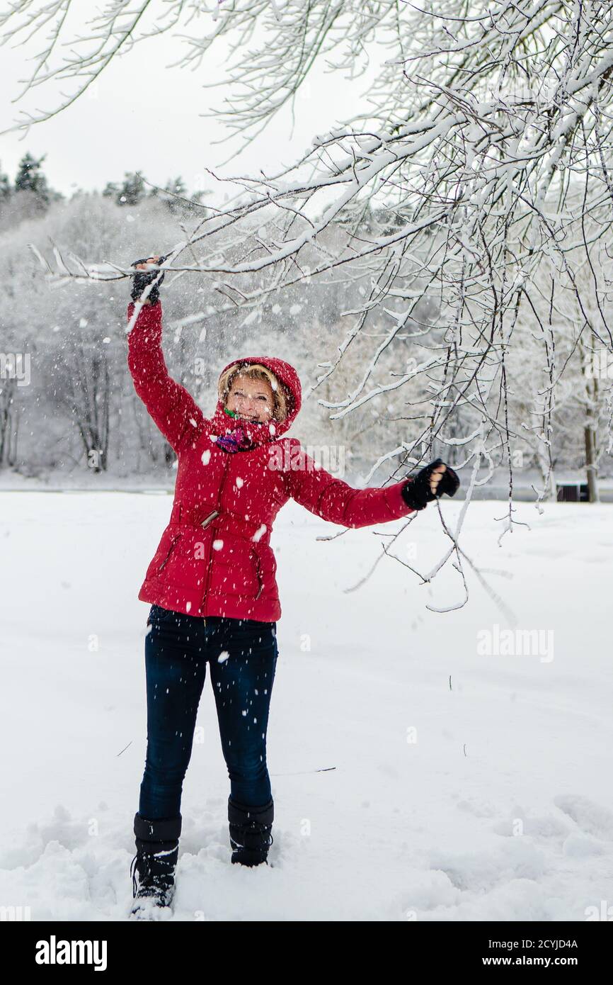 Kaukasische weiße Frau mit roter Jacke genießen verspielt am verschneiten Tag mit verschwommenem weißen Wald Hintergrund.Weihnachtszeit. Glück. Schneefälle. Stockfoto