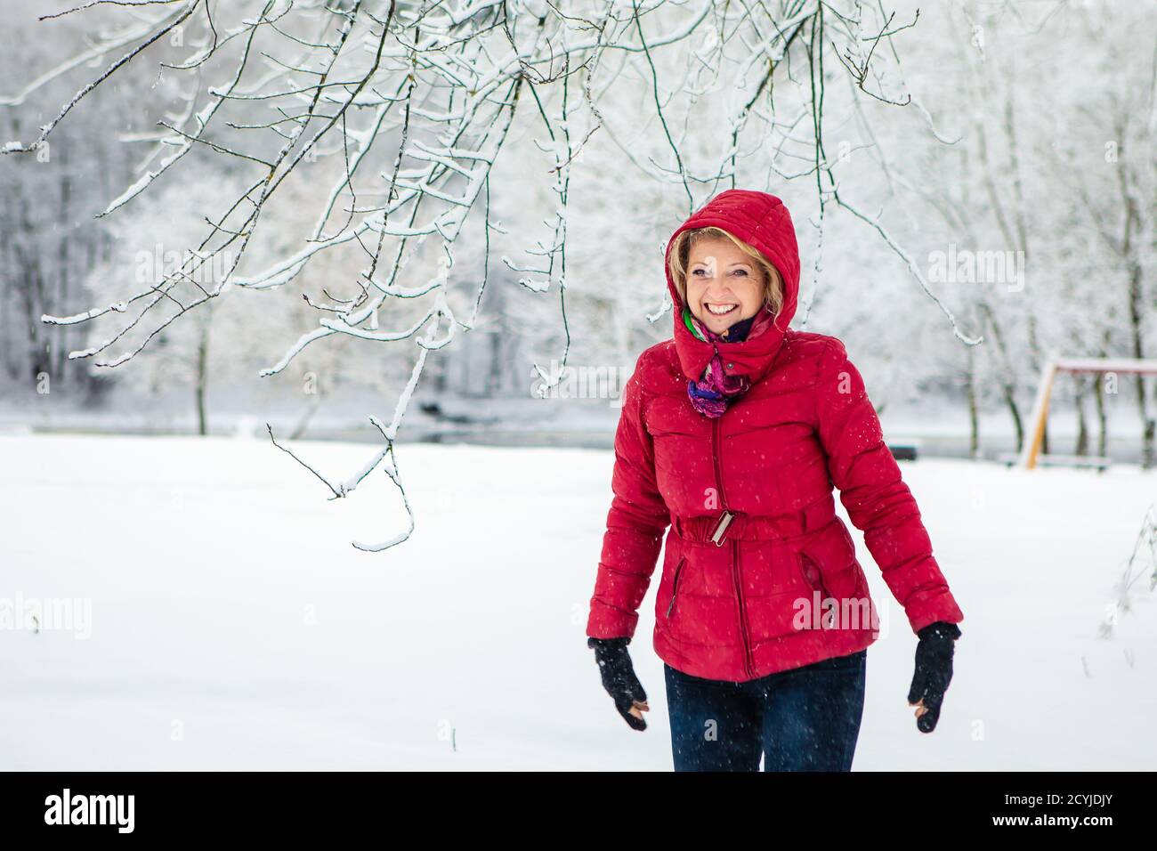 Kaukasische weiße Frau mit roter Jacke genießen verspielt am verschneiten Tag mit verschwommenem weißen Wald Hintergrund.Weihnachtszeit. Glück. Schneefälle. Stockfoto