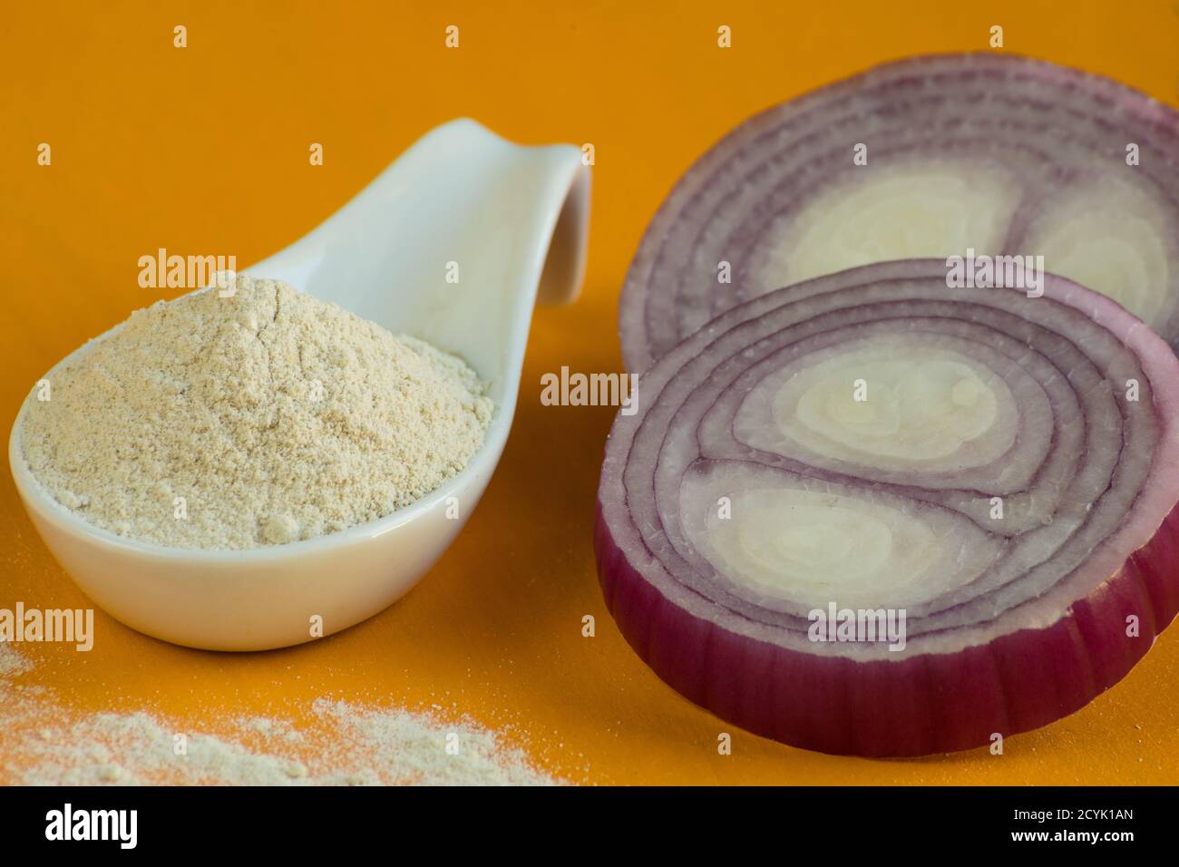 Zwiebelpulver in weißem Porzellanlöffel und roter Zwiebel auf orangefarbenem Hintergrund. Selektiver Fokus. Stockfoto