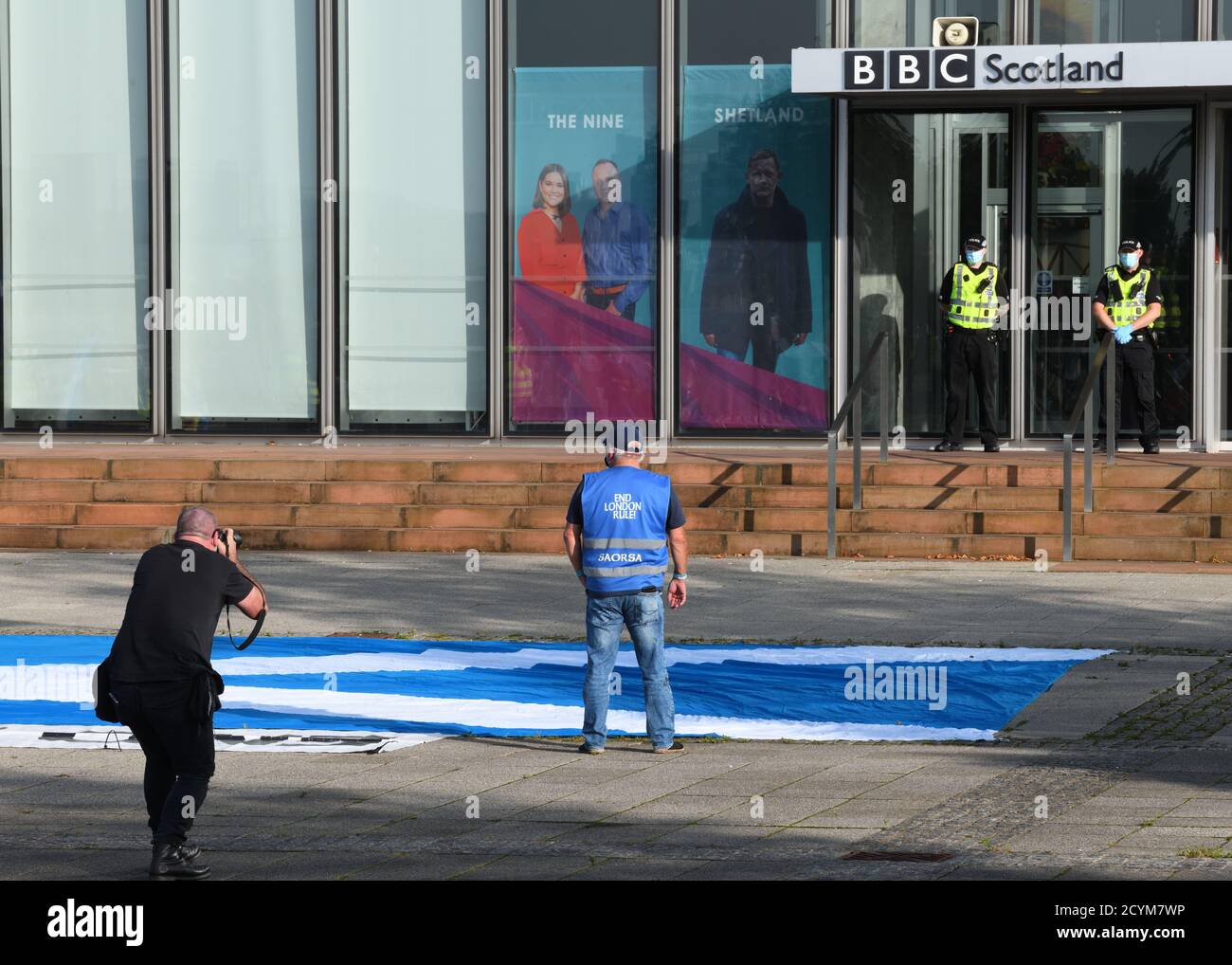 Ein einziger Protestler nach sozialer Distanzierung demonstriert gegen unlautere Berichterstattung am polizeigeschützten Eingang der BBC Scotland in Glasgow. Stockfoto